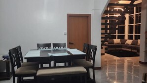 A dining area with a table and chairs, a wooden door, and a modern living space with a sofa and patterned cushions. - Little Heaven - Remarkable Spot in Georgetown (Georgetown)