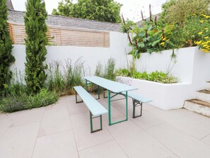 A patio with a light blue table and benches, surrounded by greenery and a white wall. - Hendre (Menai Bridge)
