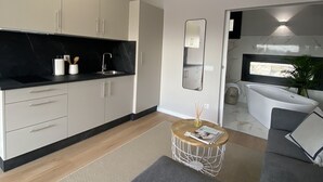 A modern kitchen with white cabinets and black countertops, a dining area with a grey sofa and a small round table, and a large window with a view of the outside. - Top Balea (O Grove)