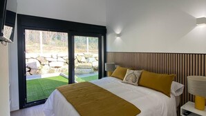 A modern bedroom with a large bed, a sliding glass door to a patio, and a wooden floor. - Top Balea (O Grove)