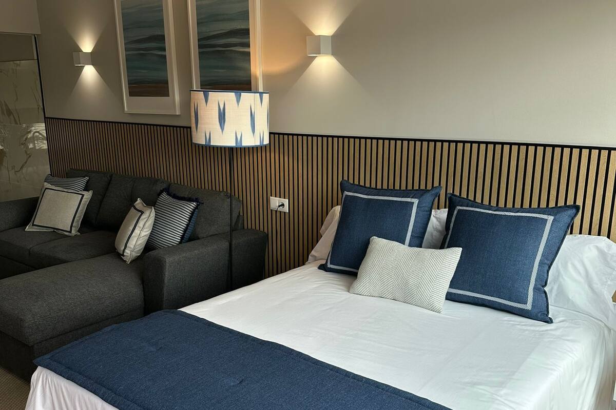 Une chambre d’hôtel avec un grand lit, un canapé et deux lampes fixées au mur.