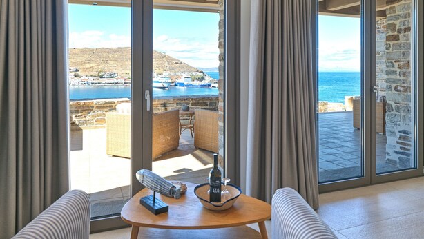 A room with a view of the sea, a table with a bottle and glasses, and wicker furniture.