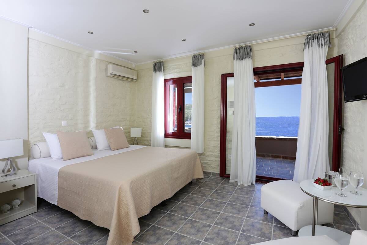 A hotel room with a bed, a small table with glasses, a TV, and a view of the sea.