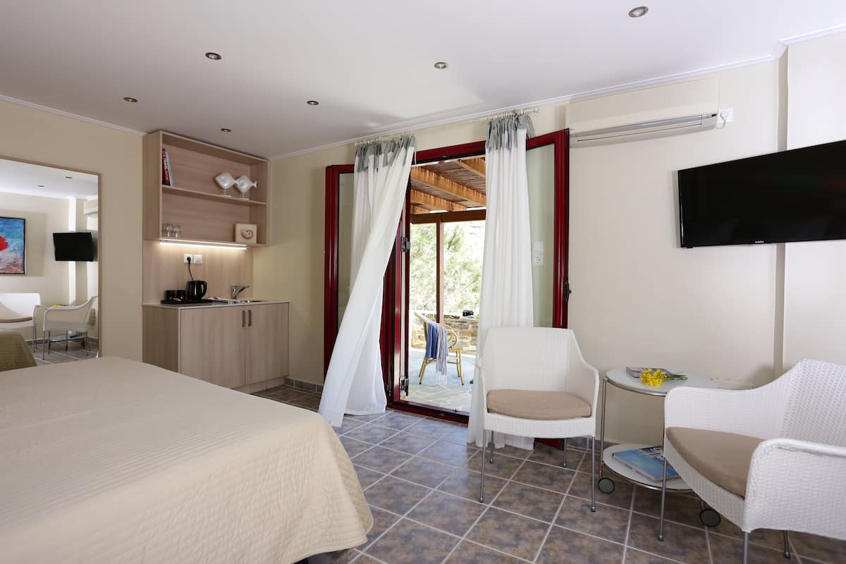 A hotel room with a bed, a desk, a chair, a TV, and a balcony with curtains.