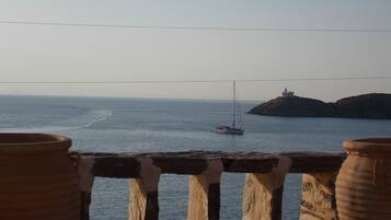 A coastal view with a sailboat on the water, a lighthouse on a hill, and large terracotta pots in the foreground.