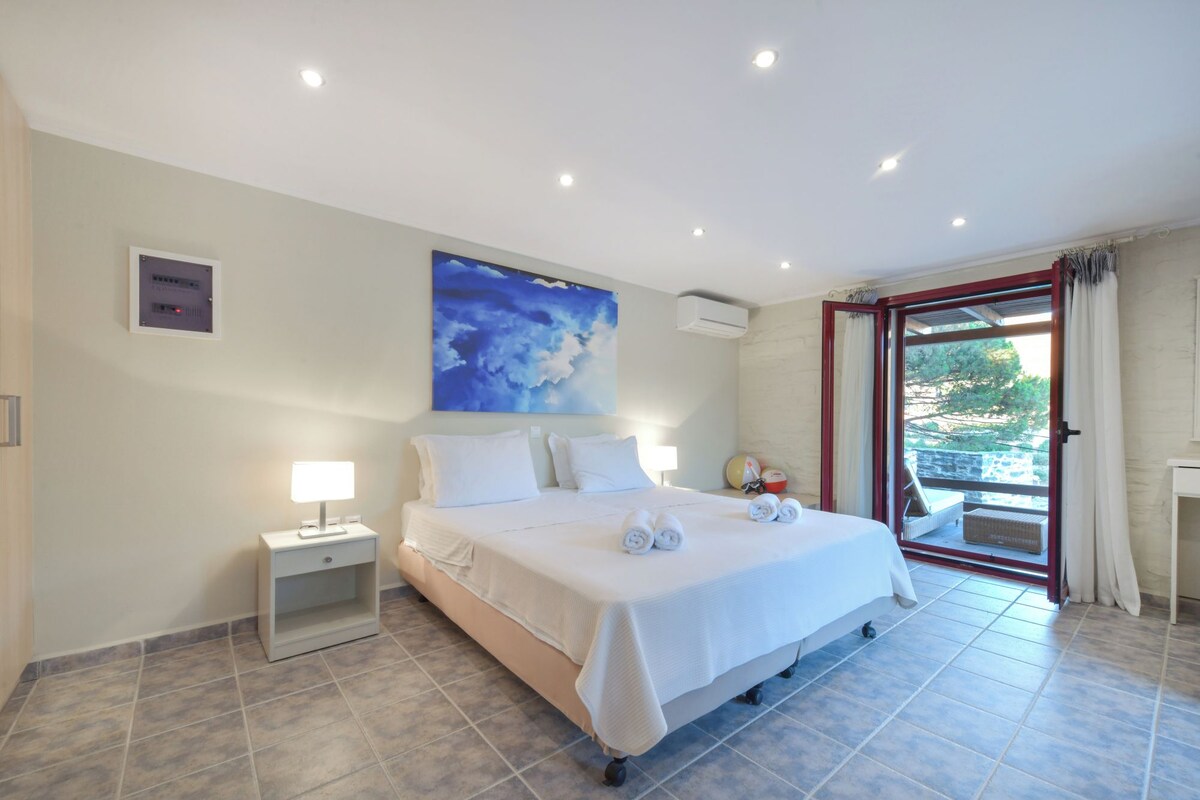 Une chambre d’hôtel avec un lit, une table de chevet, un climatiseur fixé au mur, un tableau et une vue sur l’extérieur, visible à travers une porte vitrée.