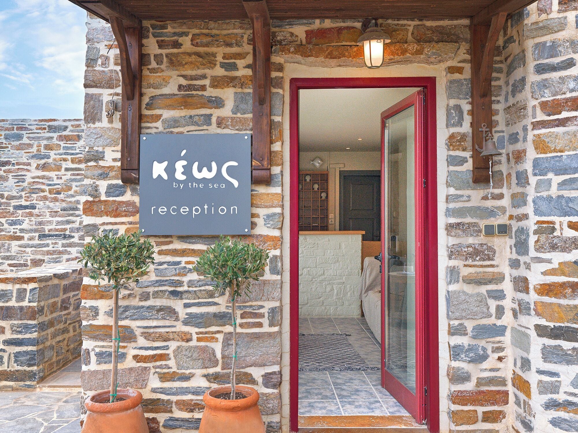 A stone building with a reception sign, a wooden door, and two potted plants.