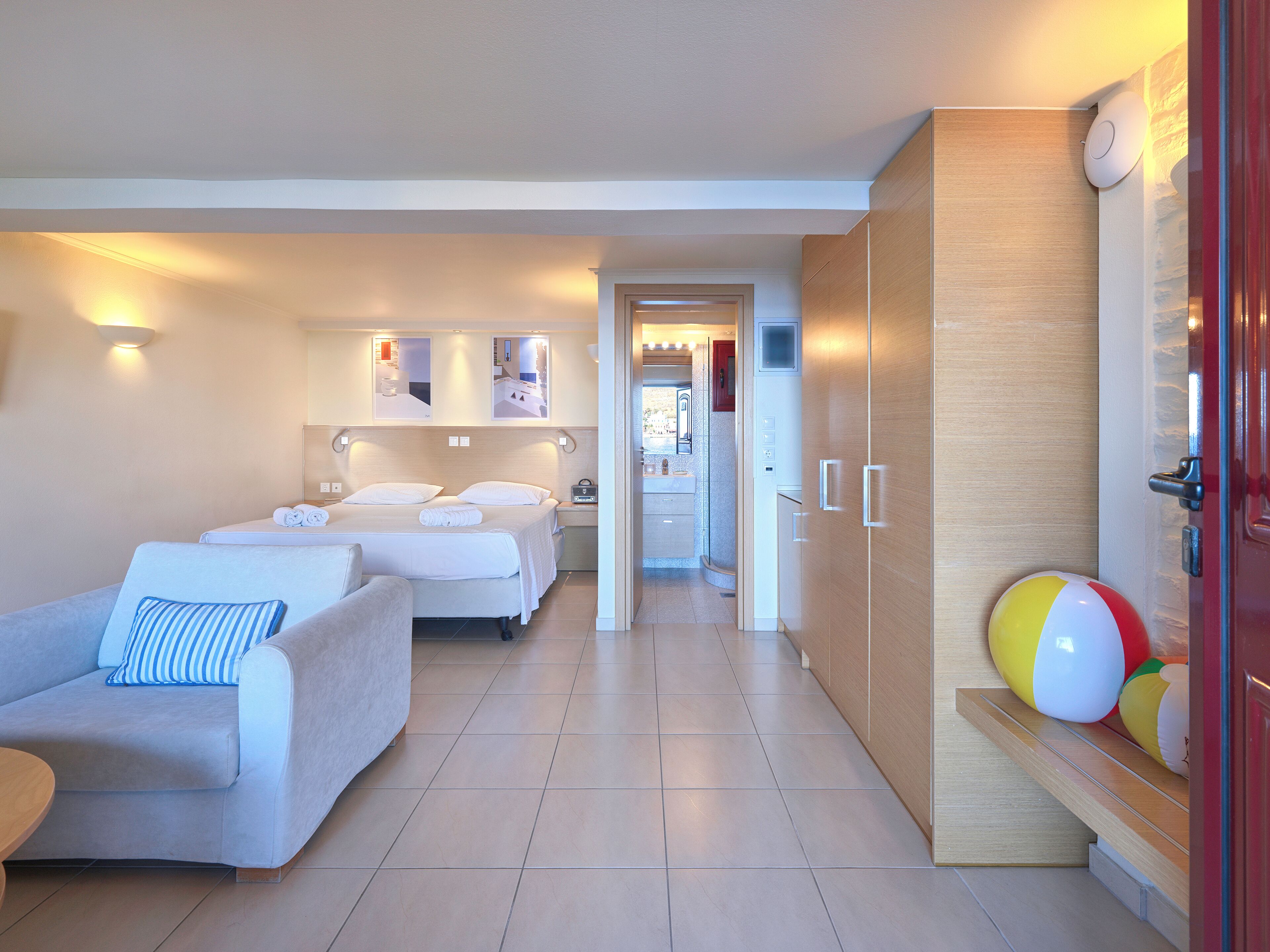 A hotel room with two beds, a sofa, a wooden wardrobe, and a small seating area.