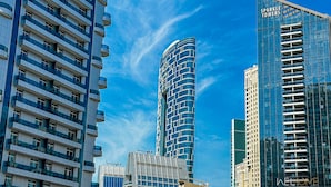 A modern high-rise building with a curved facade, multiple balconies, and a clear blue sky in the background.