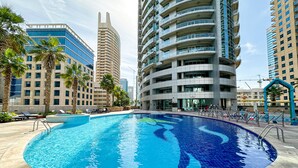 A swimming pool surrounded by high-rise buildings, palm trees, and lounge chairs.