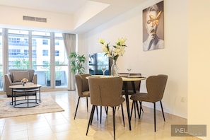 A modern living room with a dining area, large windows, and a painting on the wall.