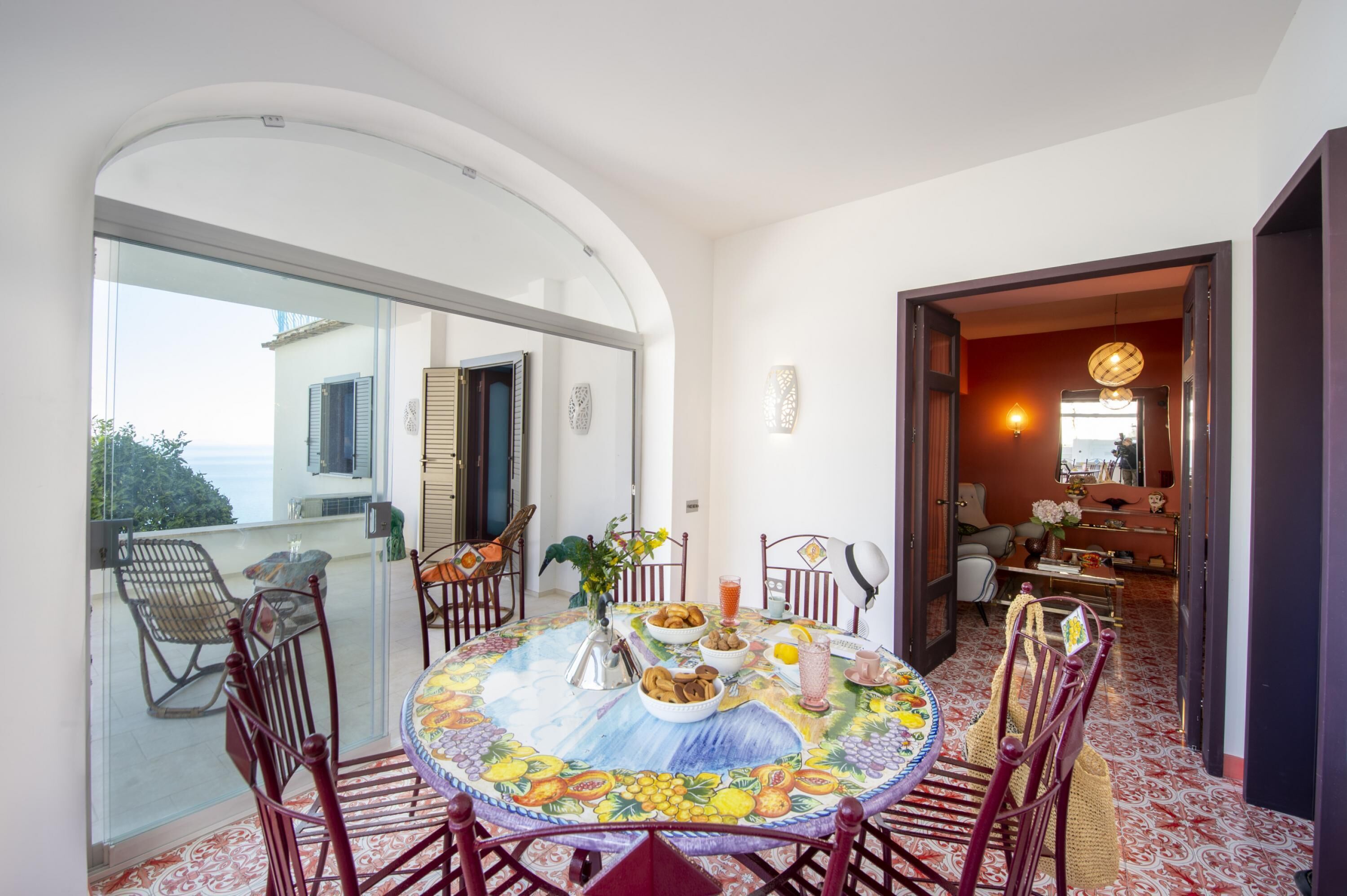 A dining area with a round table, chairs, and a view of the sea through a glass door.