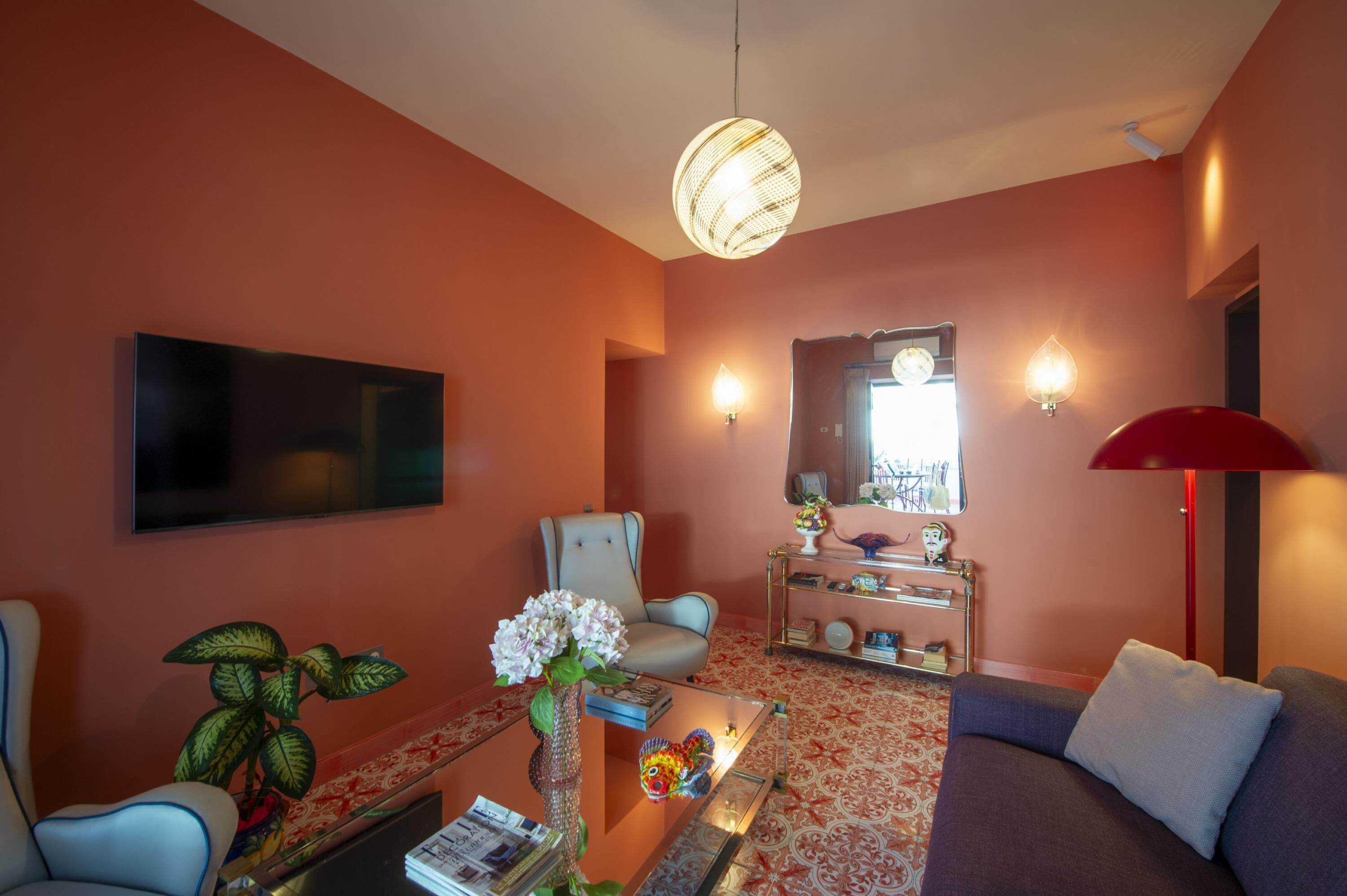 Un salon équipé d’un téléviseur à écran plat, d’un canapé confortable, d’un fauteuil, d’une table basse agrémentée d’objets décoratifs et d’une lampe rouge.