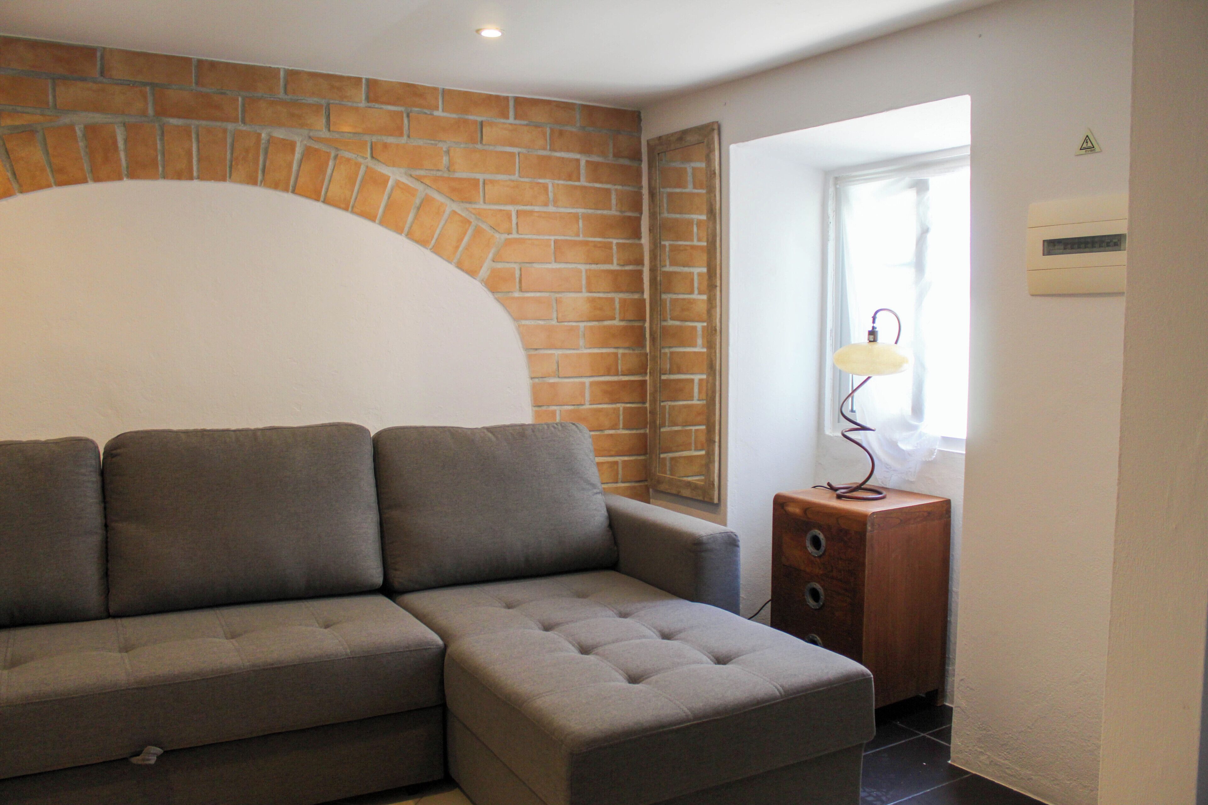 A modern living room with a sectional sofa, a wooden cabinet, and a brick accent wall.