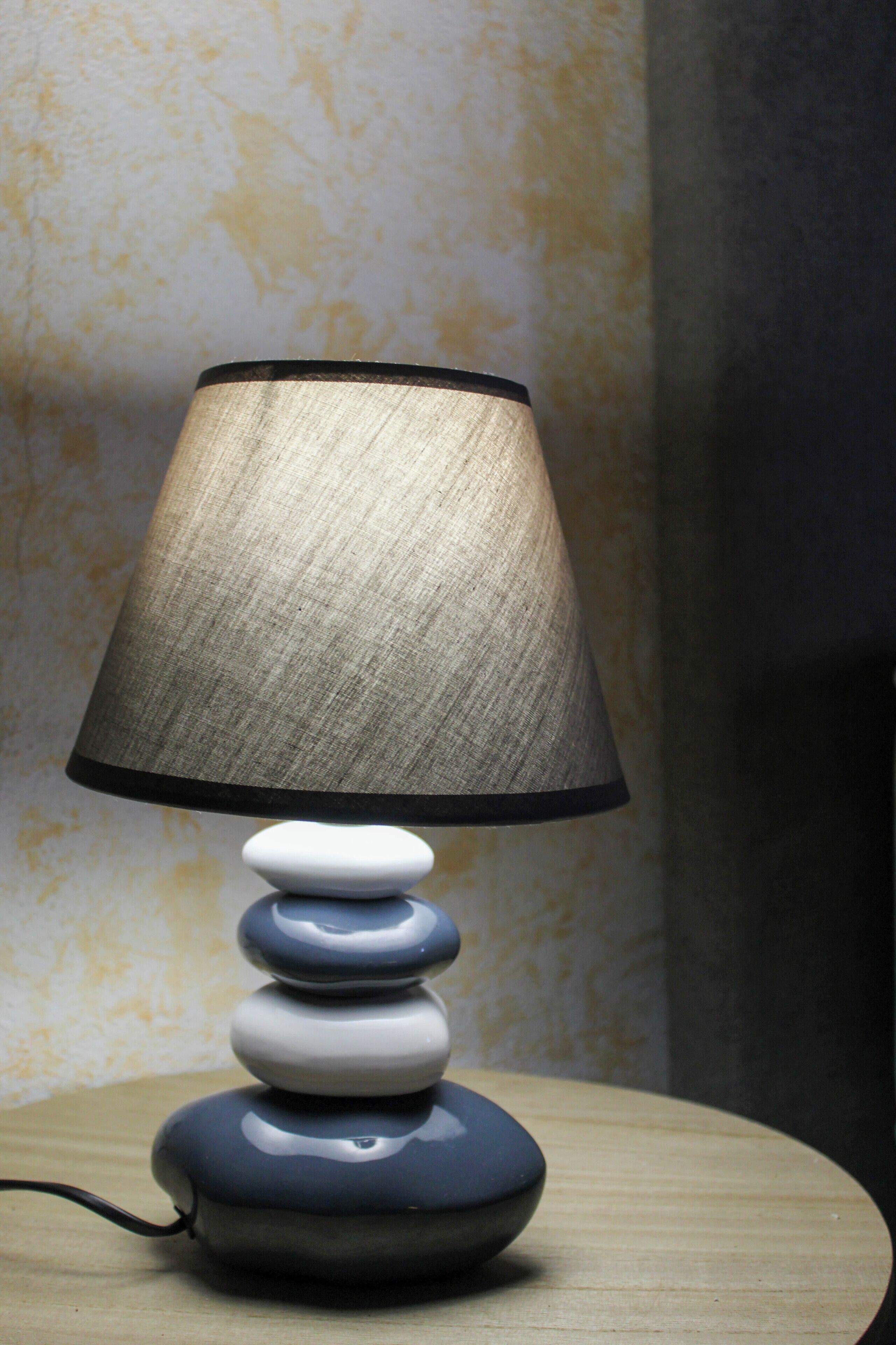 A lamp with a textured shade and a stacked base on a wooden surface.