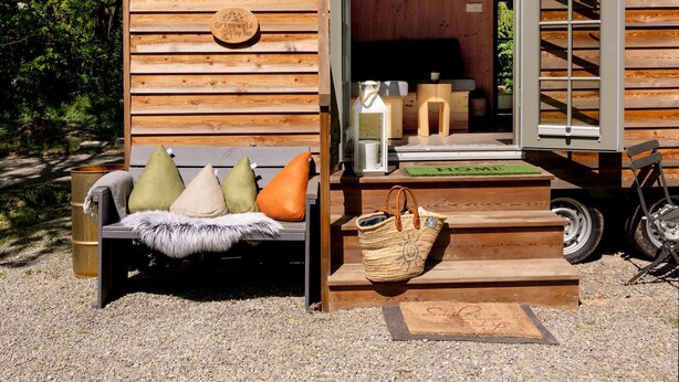 A wooden cabin with a sliding door, a sofa with cushions, and a small outdoor seating area. - Märchenhaftes Tiny Haus auf dem Historischen Gut Junkernhof in der Grimm Heimat (Calden)