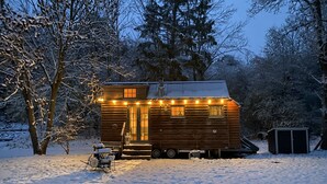 A wooden cabin with a covered porch and a small deck, surrounded by snow-covered trees. - Märchenhaftes Tiny Haus auf dem Historischen Gut Junkernhof in der Grimm Heimat (Calden)