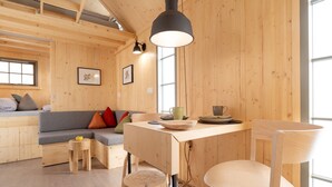 A cozy wooden cabin interior with a dining table, chairs, a sofa with cushions, and a hanging light fixture. - Märchenhaftes Tiny Haus auf dem Historischen Gut Junkernhof in der Grimm Heimat (Calden)