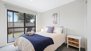A bedroom with a large window, a bed with a blue blanket, a bedside table with baskets, and a wall-mounted picture. - Beachside Escape in Cowes (Cowes)