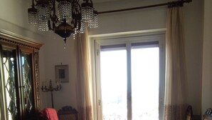 A bedroom with a large bed, a chandelier, a window with curtains, and a view of the outside.