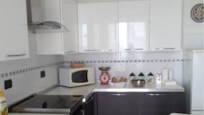 A compact kitchen with white cabinets, a microwave, a stove, and a sink.