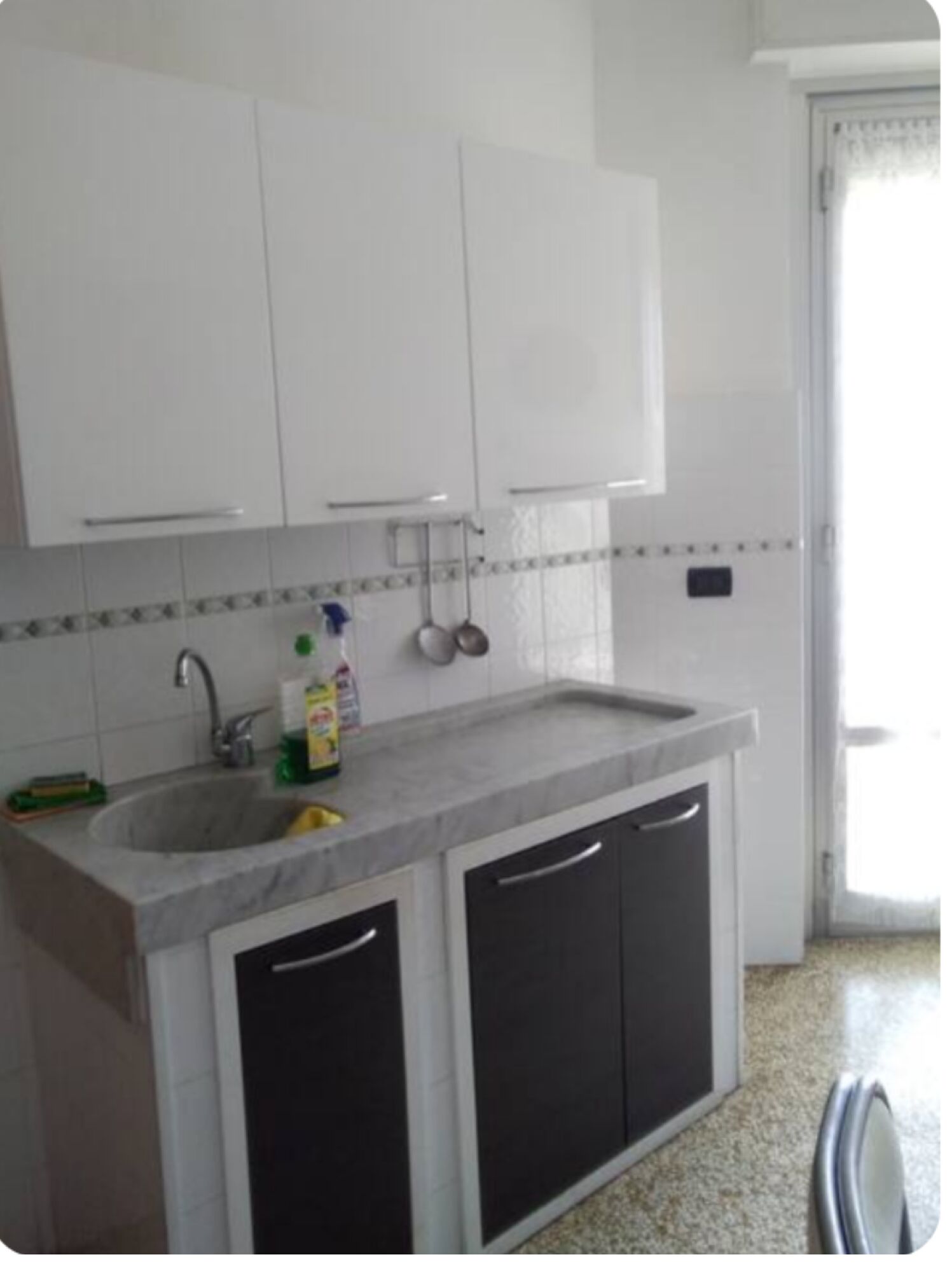A kitchen with white cabinets, a marble countertop, and a sink.