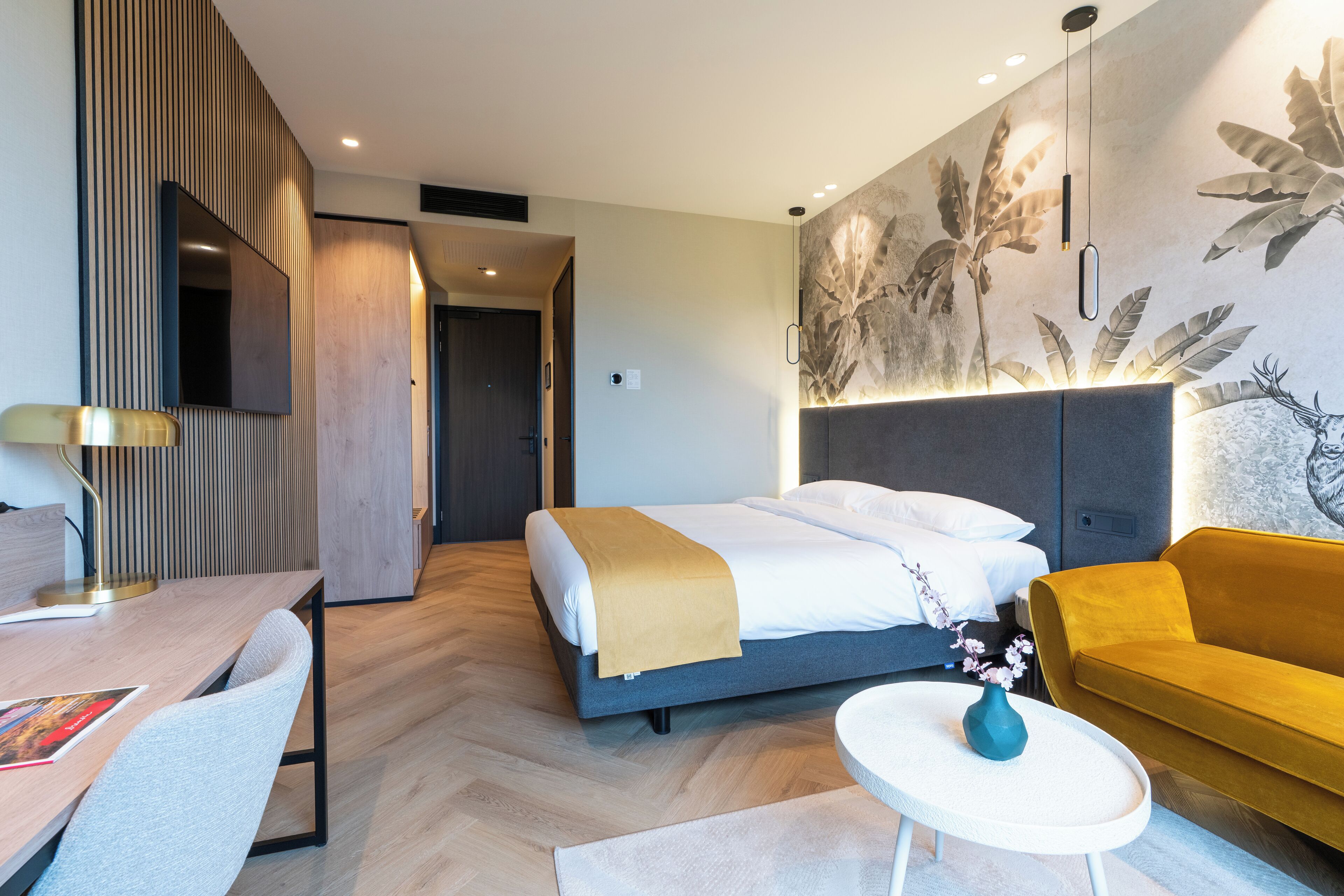 Una habitación de hotel moderna con cama, sofá, escritorio y televisor montado en la pared.