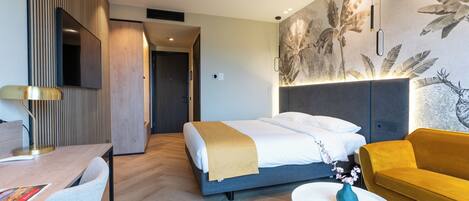 Una habitación de hotel moderna con cama, sofá, escritorio y televisor montado en la pared.