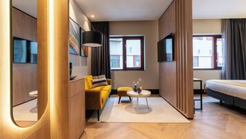 A modern hotel room with a wooden floor, a yellow sofa, a round table, and a bed.