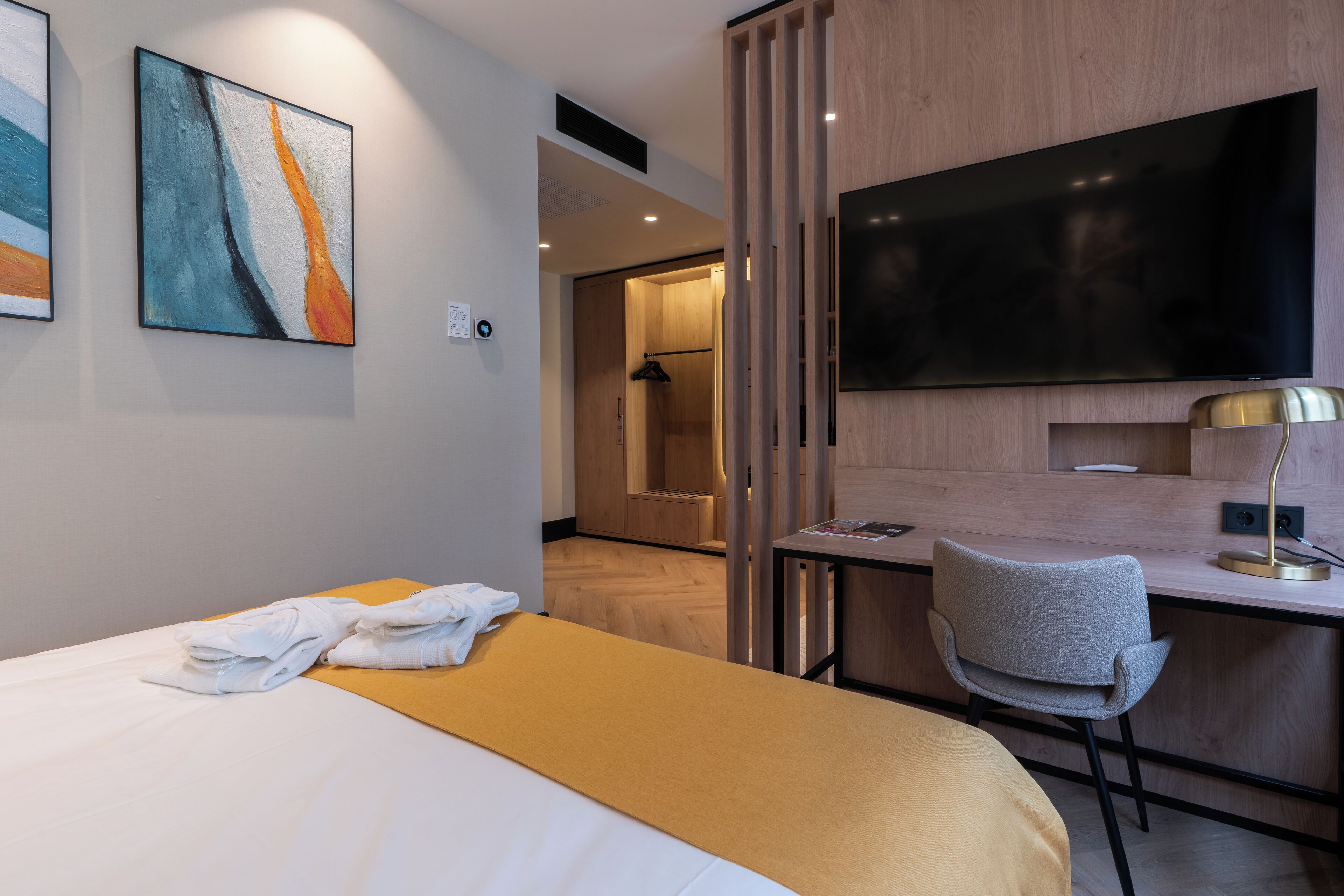 Ein Hotelzimmer mit Bett, Schreibtisch, Sessel, Fernseher und Bildern an der Wand.