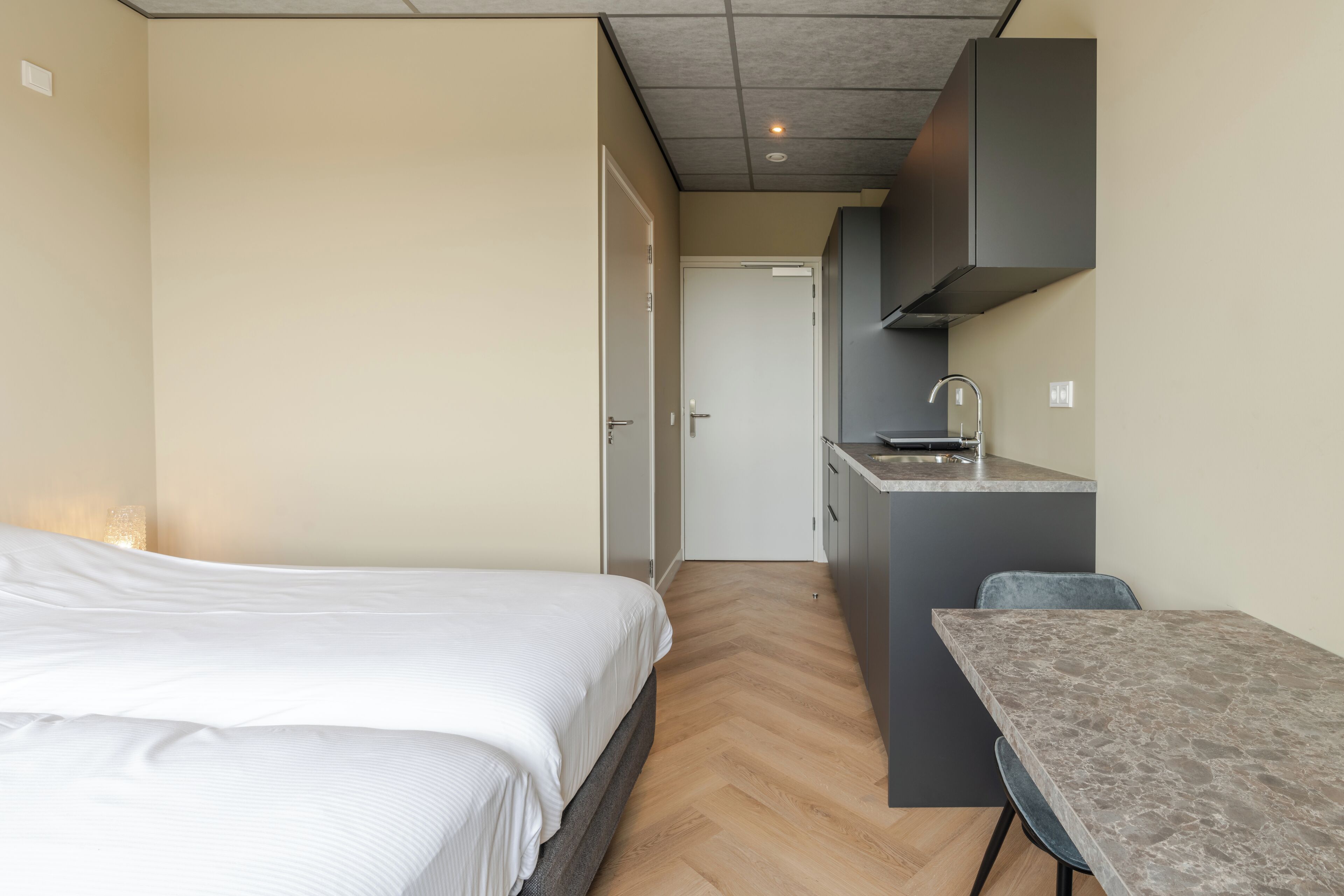 A bedroom with a bed, a small kitchenette with a sink, and a dining area with a table and chairs.