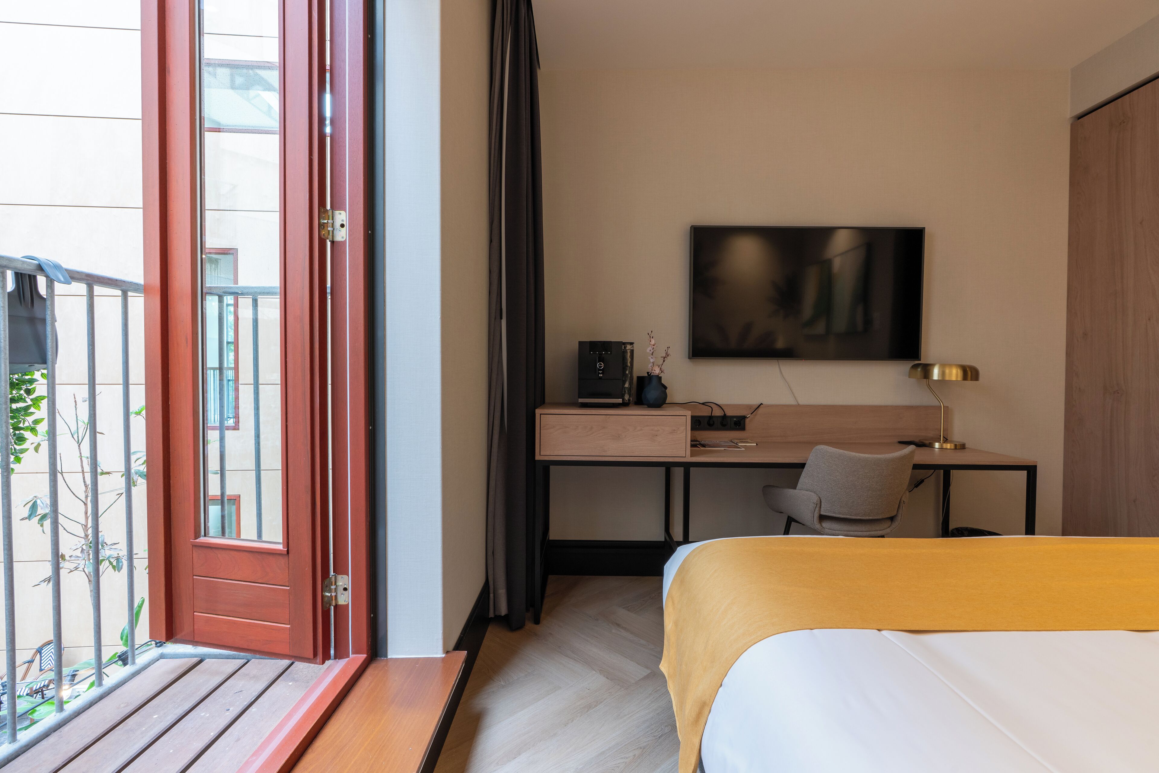 A hotel room with a bed, desk, chair, TV, and a balcony with a door.