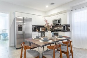 A modern kitchen with white cabinets, stainless steel appliances, and a wooden dining table with four chairs. - Cherry Suites 3BR Apt w W D Pool Table (Philadelphia)