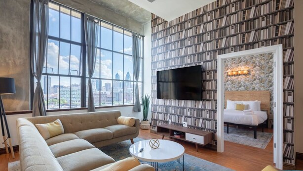 A modern living room with a large sofa, a coffee table, and a bookshelf filled with books. - Sosuite 2BR Penthouse w W D Gym On-site Bar (Philadelphia)
