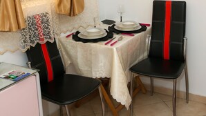 A dining area with a table set for two, chairs with red accents, a small cabinet, and two framed pictures on the wall. - Conte Studio (Corfu)
