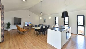 Eine moderne Küche mit Kochinsel, Essbereich mit Stühlen, einem Fernseher und einem Blumentopf.