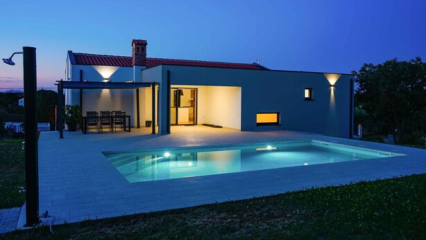 Ein modernes Haus mit Swimmingpool, einer Terrasse und Gartenmöbeln sowie einem gut beleuchteten Eingangsbereich.