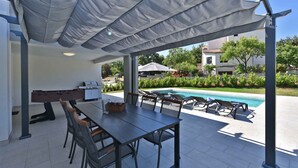 Eine Außenpatio mit Pool, Grill und Tisch mit Stühlen.