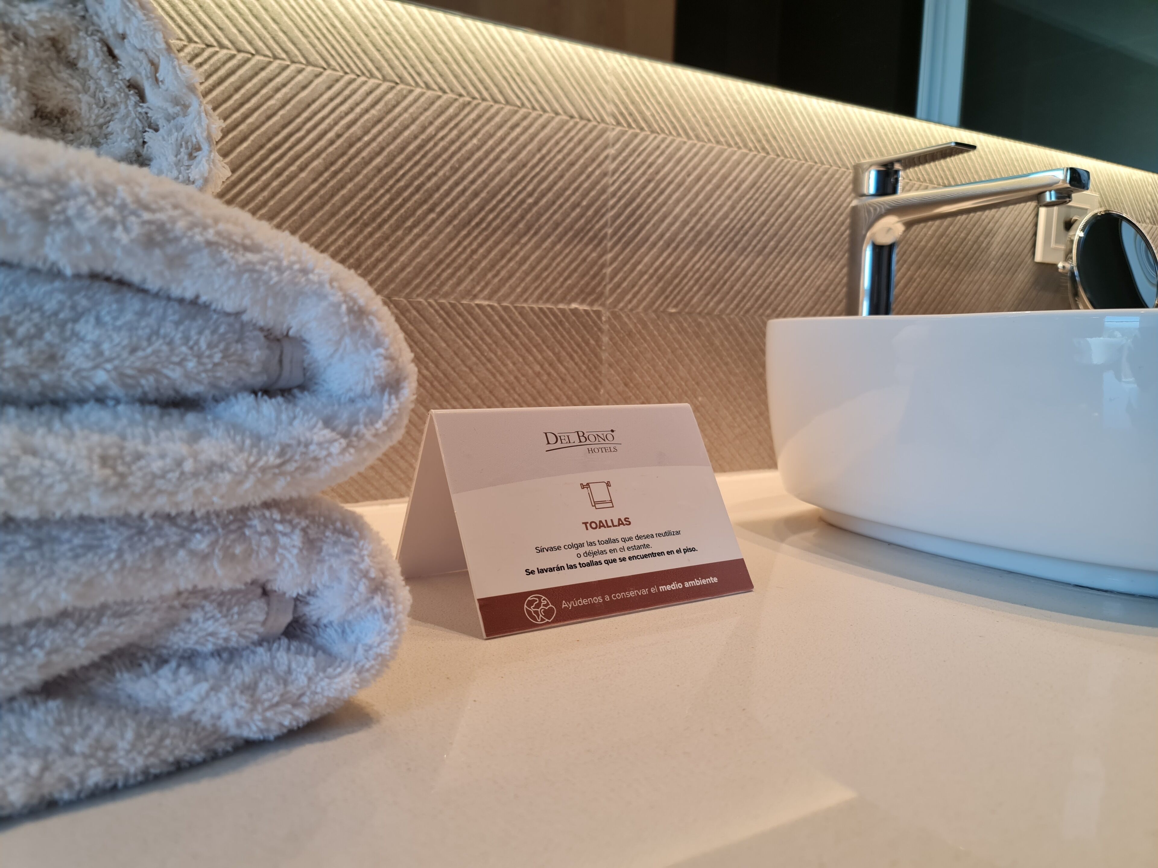A hotel bathroom with a towel rack, a sink, and a sign indicating towel usage instructions.