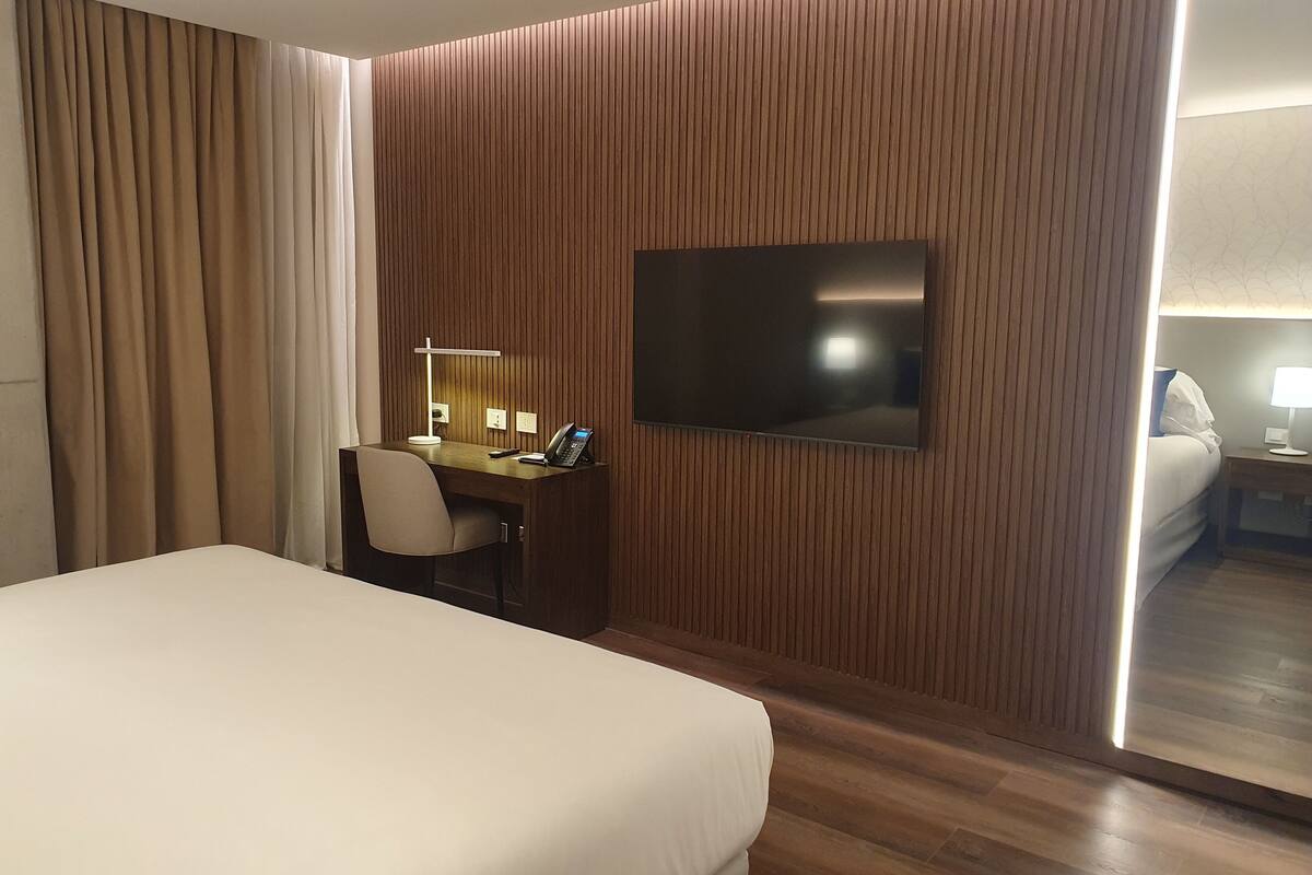 Une chambre d’hôtel équipée d’un lit, d’un bureau avec un téléphone, d’un téléviseur à écran plat et d’un miroir.
