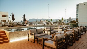 A rooftop pool area with lounge chairs, a wooden deck, and a view of the city skyline. - Hotel Del Bono Central (San Juan)