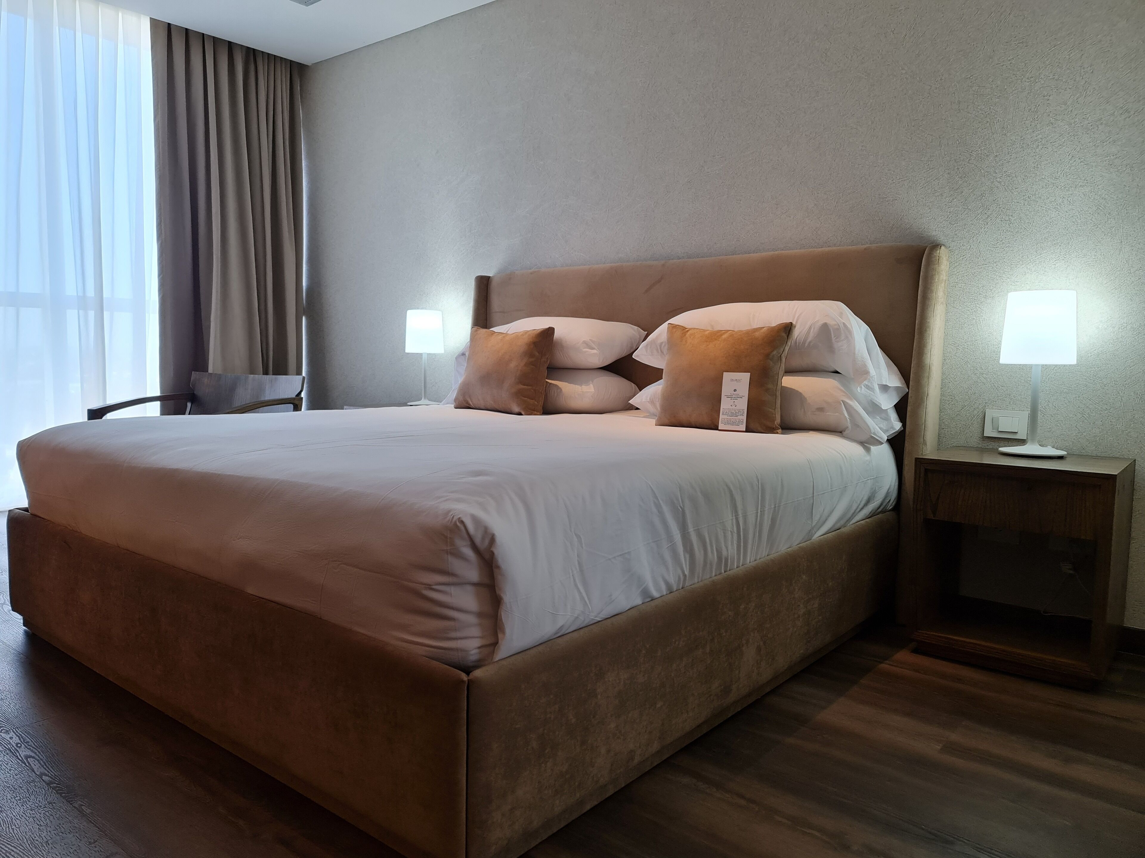 A large bed with a headboard, two bedside tables with lamps, and a chair.