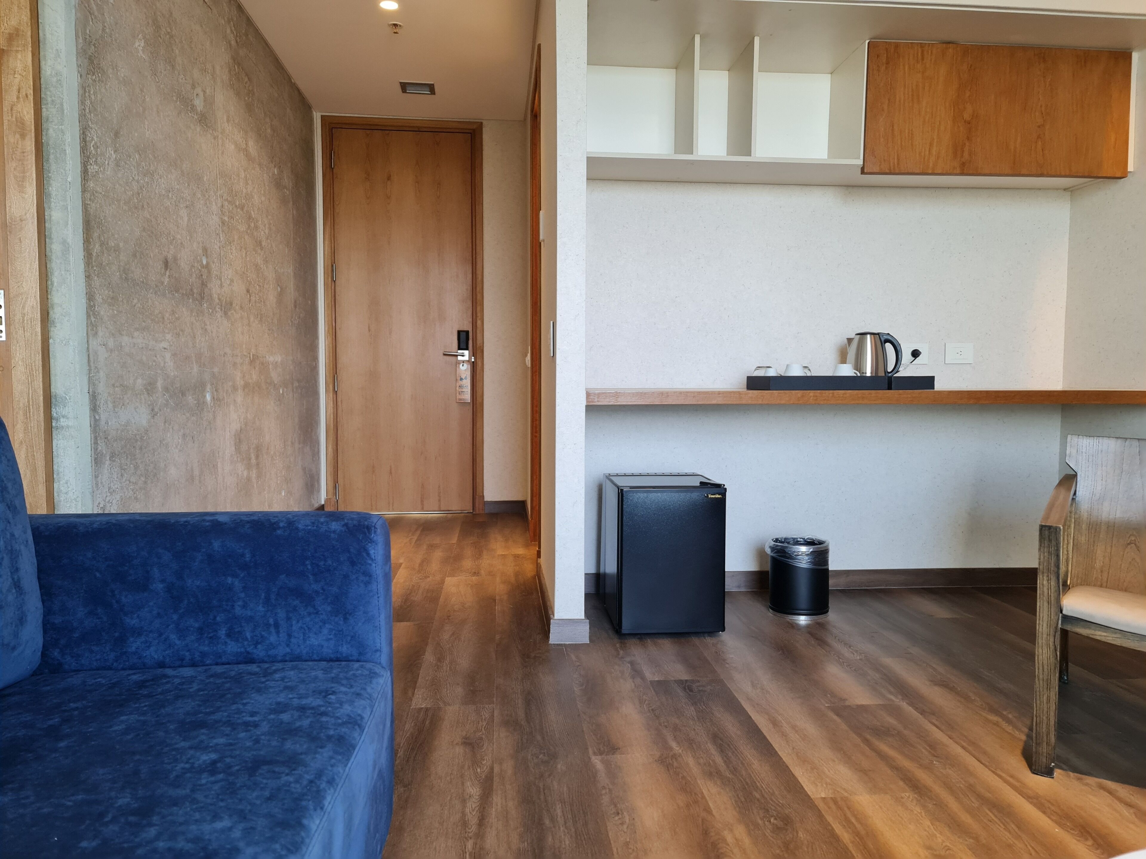 Una habitación moderna con un sofá azul, una puerta de madera, un refrigerador negro pequeño y un cubo de basura.