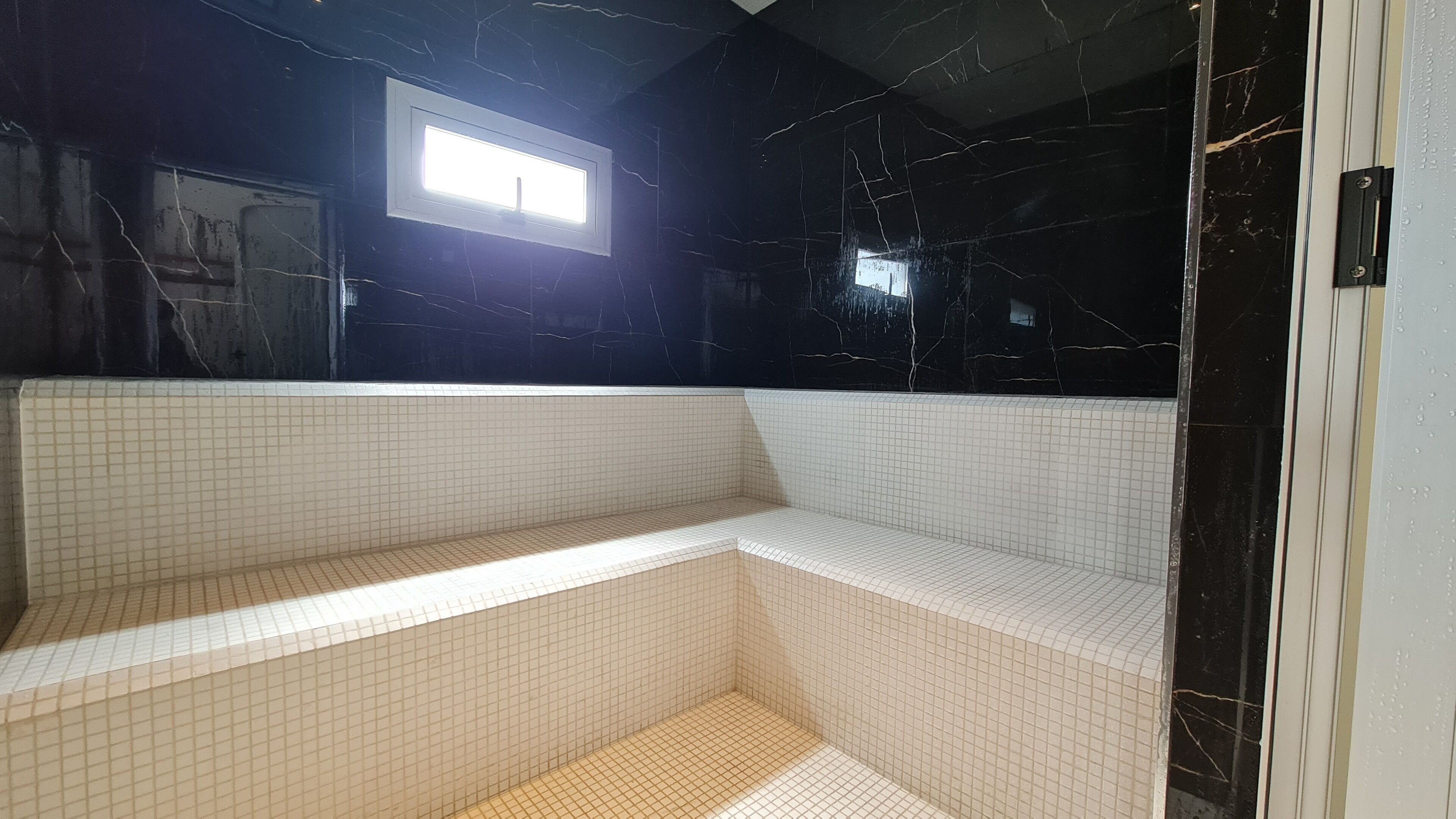 Ein Badezimmer mit schwarzer Marmorwand, weiß gefliestem Sitzbrett und einem kleinen Fenster.