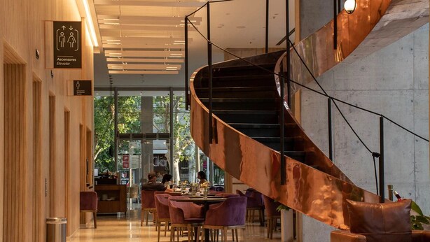 A modern interior with a spiral staircase, wooden paneling, and a dining area with purple chairs. - Hotel Del Bono Central (San Juan)