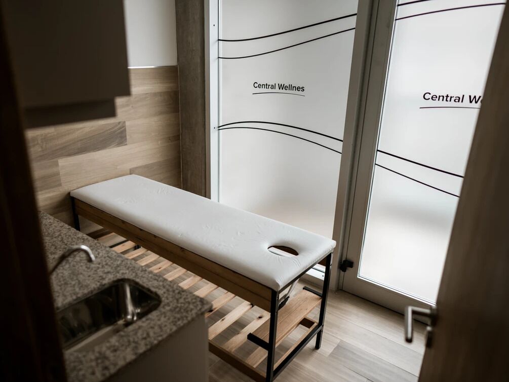 A modern bathroom with a bench, a sink, and frosted glass doors labeled "Central Wellness".