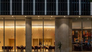 A modern building with a glass facade, large columns, and a seating area with tables and chairs. - Hotel Del Bono Central (San Juan)