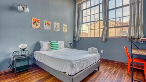 Une chambre à coucher avec un lit, un bureau, une chaise, une lampe et des œuvres d’art accrochées au mur.