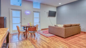 Un salon moderne avec un plancher en bois, un canapé marron, une table à manger avec des chaises et un panneau lumineux au néon.