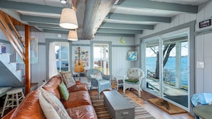 Een gezellige woonkamer met een leren bank, een blauwe stoel en een houten tafel. Er is een groot raam met uitzicht op het water.